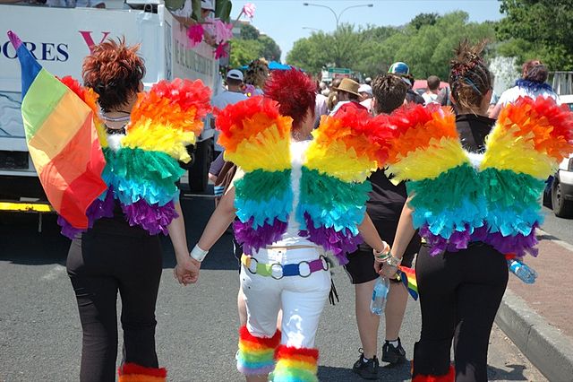 Three people wearing rainbow wings facing away from camera.