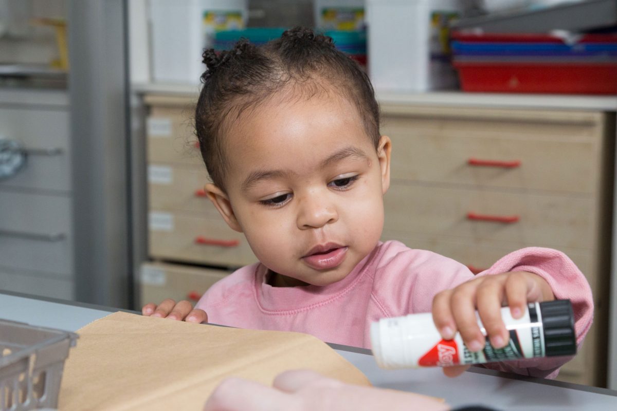 A young girl is at a table holding a pritt stick of glue