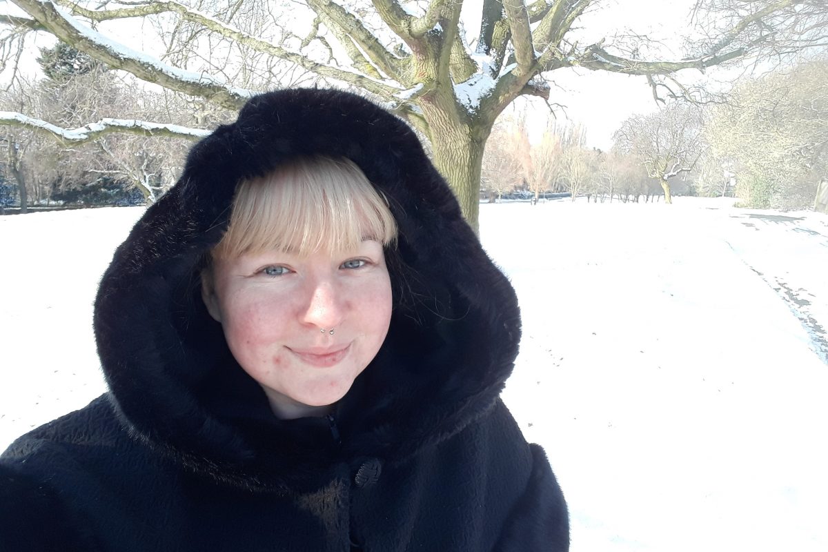 Female in black fax fur coat standing gardens filled with snow.