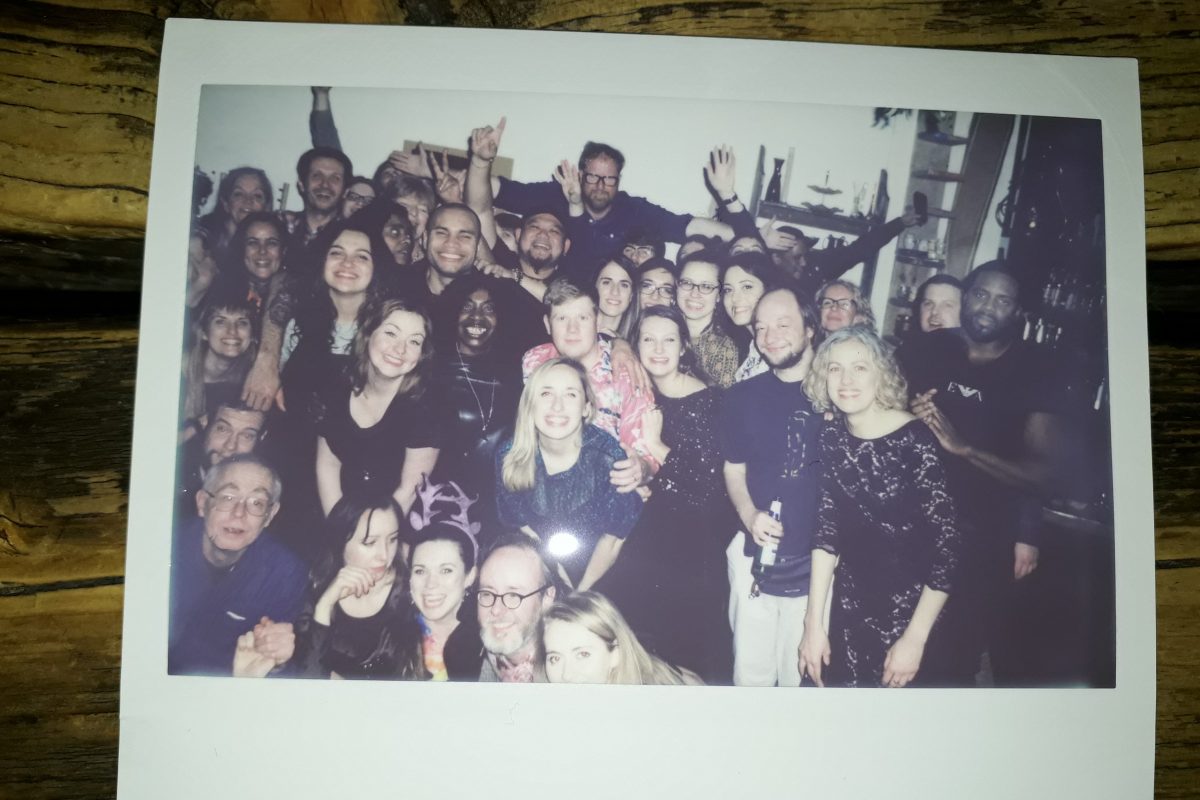 A Polaroid with a large group of men and women gathered together smiling