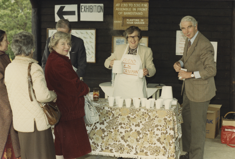 Woman and man pose for camera at a stall, three women are waiting for tea. One lady is turned to smile at the camera.