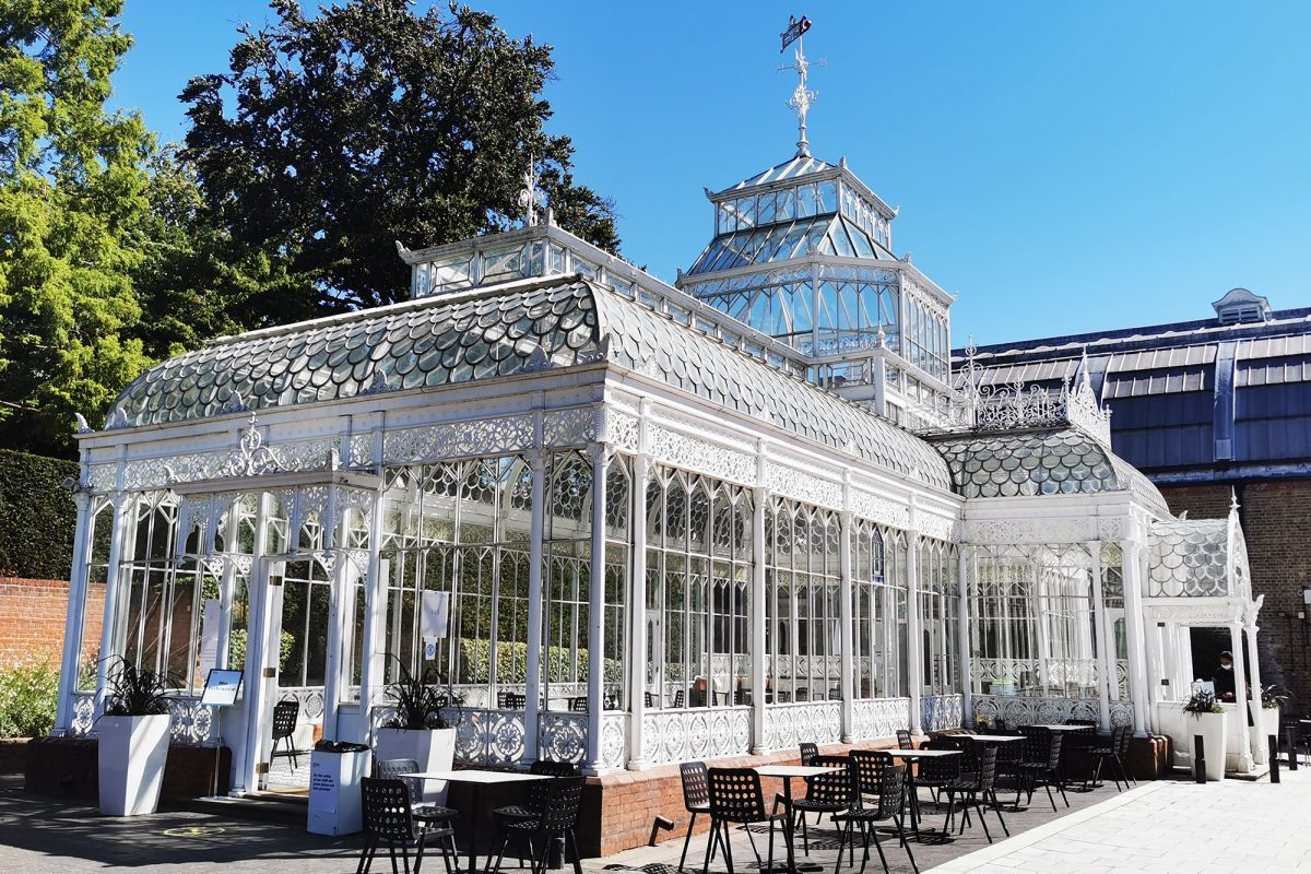 Glass building with seating and tables outside. Clear sunny day.