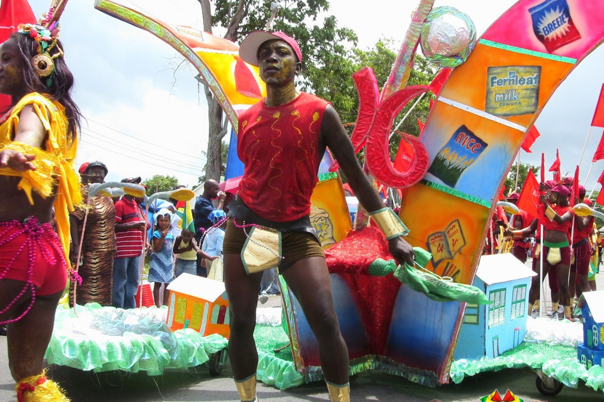 Man in colourful parade outfit, crowds of people watching at side of street.