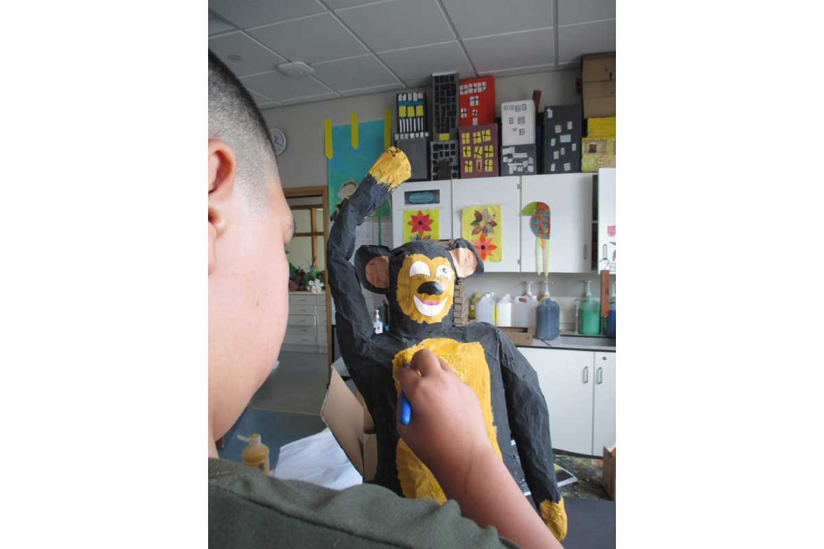 A student at Drumbeat School paints a papier mache monkey