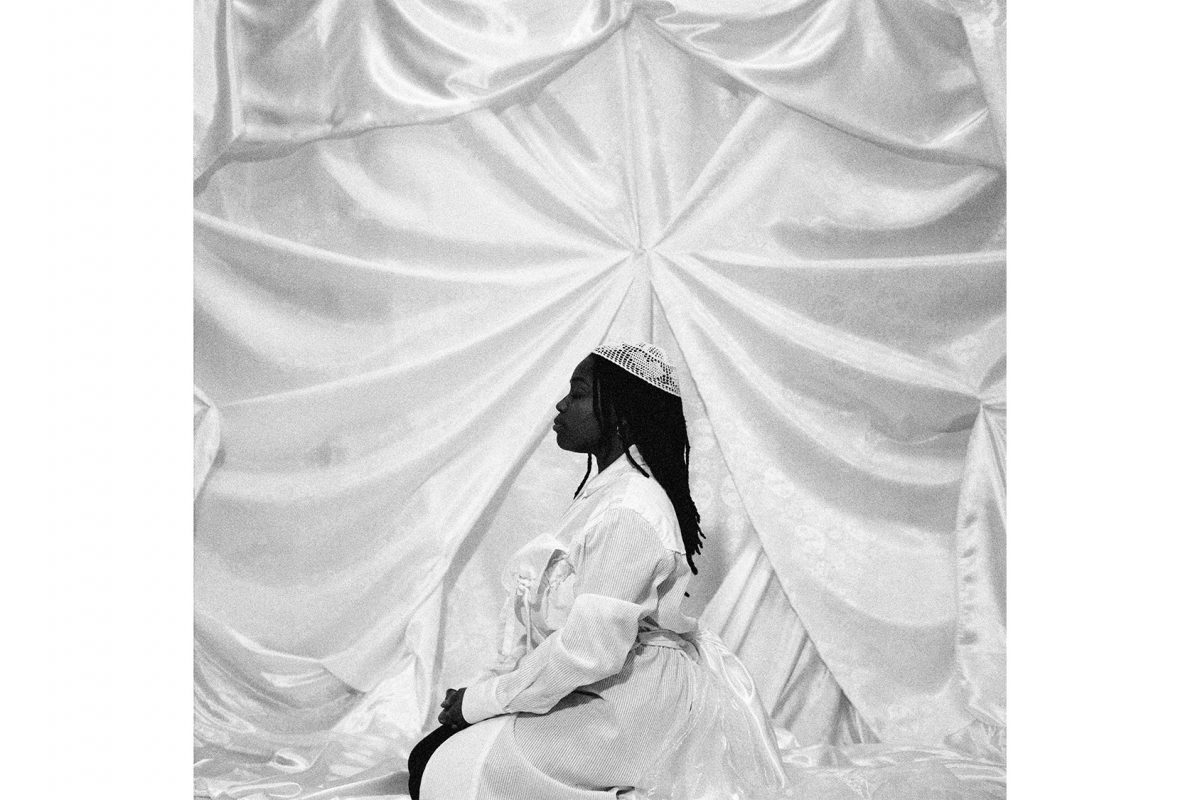 Woman sitting on knees wearing white dress.