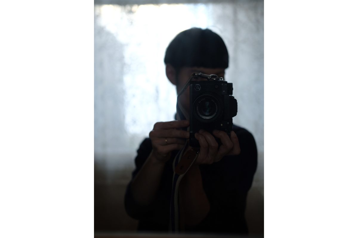 A woman takes a photo of herself in a mirror with a camera, we can see that she has a bowl cut haircut