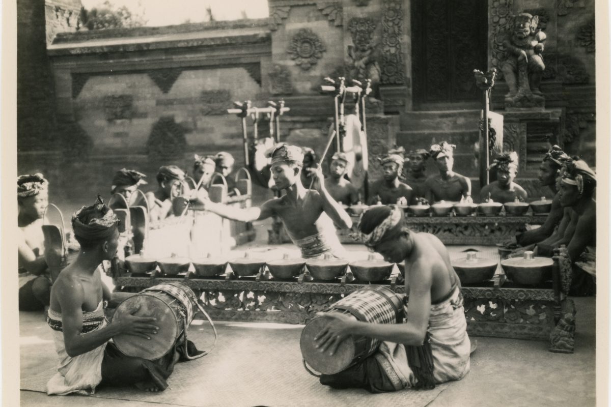 Archive photo of a group of Balinese men, with two in the foreground playing drums and one in the centre playing a row of drums