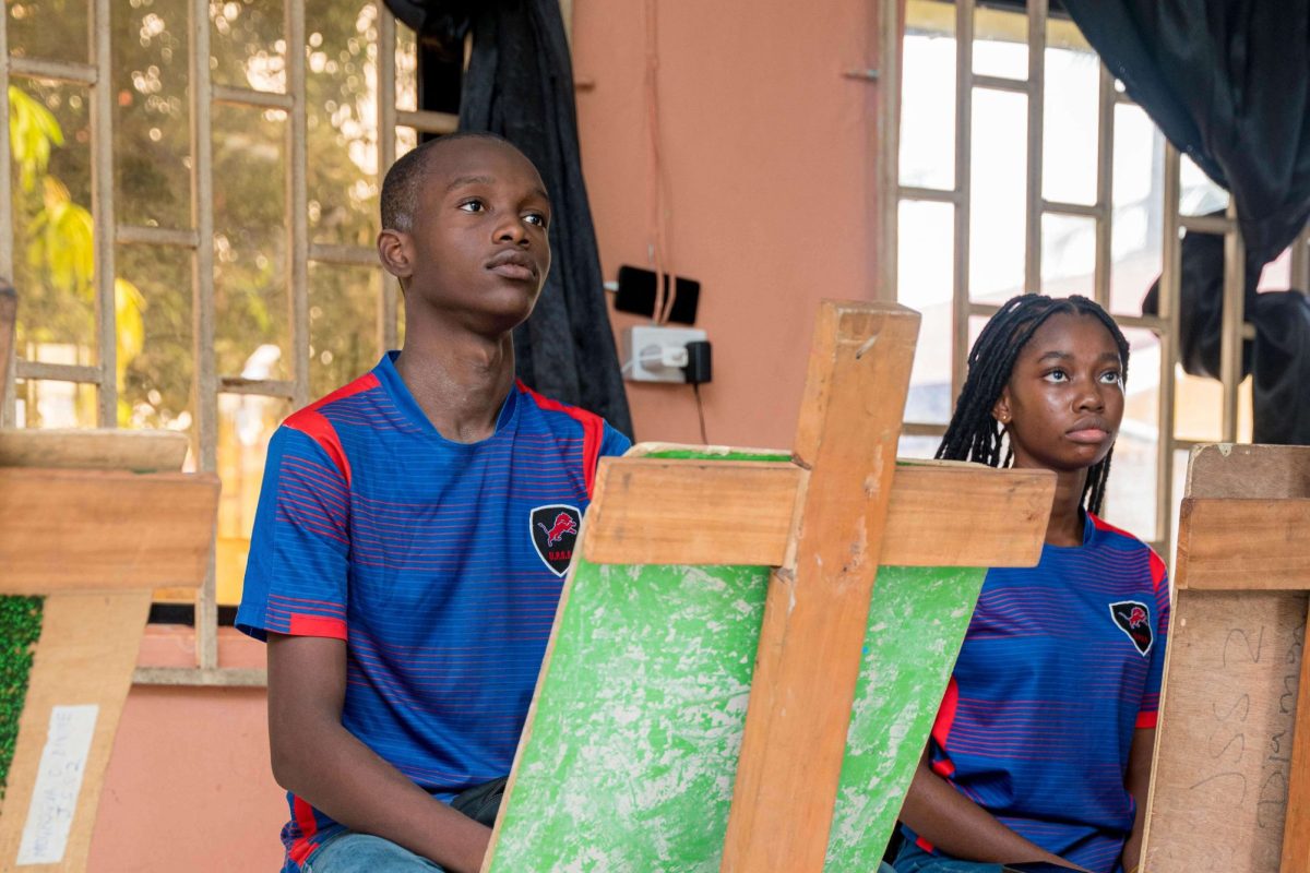 Two teenage school children sit behind easels and look at a teacher slightly off camera