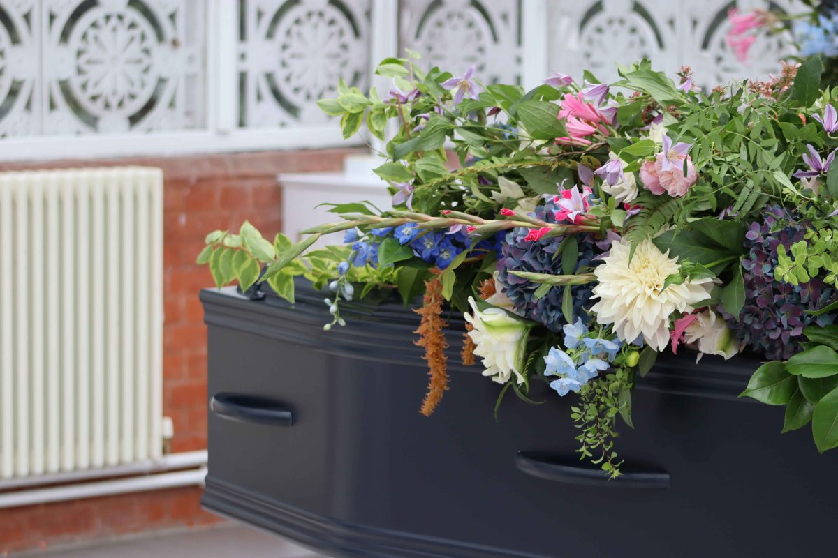 The corner of a blue coffin, topped with wild flowers